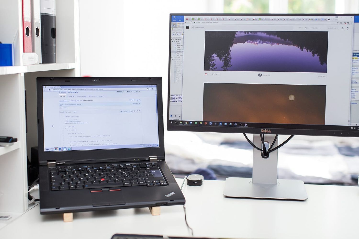 Laptop mit PHP-Code auf GitHub neben einem großen Monitor auf hellem Schreibtisch