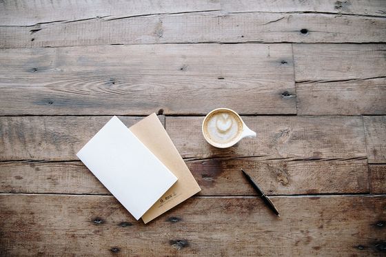 Zwei Notizhefte, Kugelschreiber und Cappuccino auf einem rustikalen Holztisch von oben