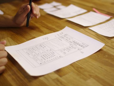 Handgezeichneter Papierprototyp einer Website-Oberfläche auf einem Holztisch, daneben weitere Skizzen