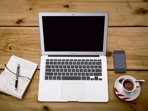 Laptop, Smartphone, Espresso und Notizbuch mit App-Skizzen auf einem Holztisch