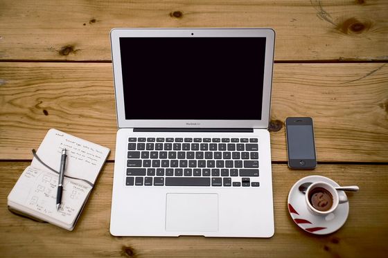 Laptop, Smartphone, Espresso und Notizbuch mit App-Skizzen auf einem Holztisch